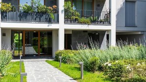 A multi-story residential building with balconies, a stone pathway, and surrounding greenery. - Stylish Apartment With Terrace and Swimming Pool (Milan)