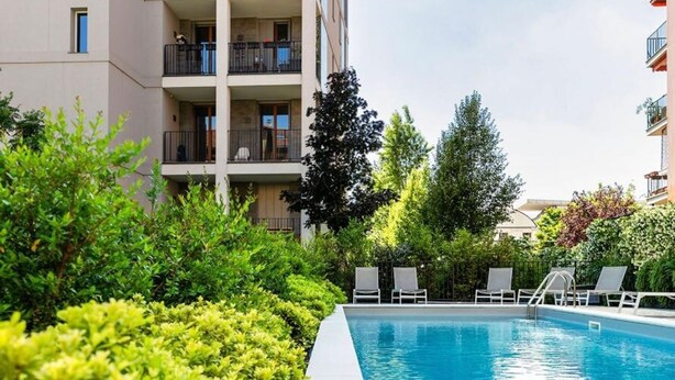 A swimming pool with lounge chairs, surrounded by greenery and adjacent to a multi-story building. - Stylish Apartment With Terrace and Swimming Pool (Milan)