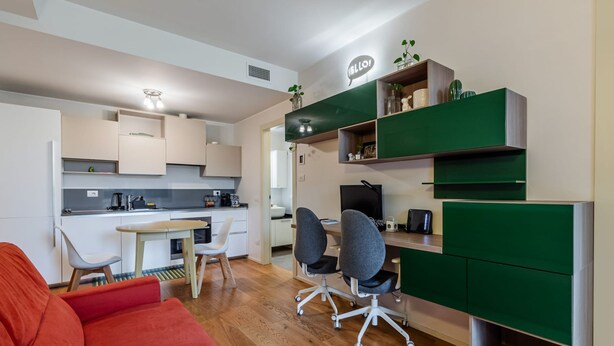 Una cocina moderna con armarios blancos, una zona de comedor con sofá rojo y un espacio de trabajo con estanterías verdes.