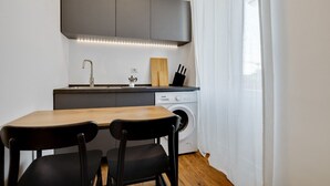 A compact kitchen with a wooden table and two chairs, a washing machine, and a built-in cabinet above the sink. - Cozy Penthouse With Stunning View Balcony (Milan)