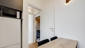 A compact kitchen with a built-in microwave, a white refrigerator, and a wooden dining table with black chairs. - Cozy Penthouse With Stunning View Balcony (Milan)