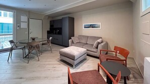 A modern living room with a grey sofa, a dining table with chairs, and a kitchen area with dark cabinets. - Modern Apartment in the Heart of Pisa (Pisa)