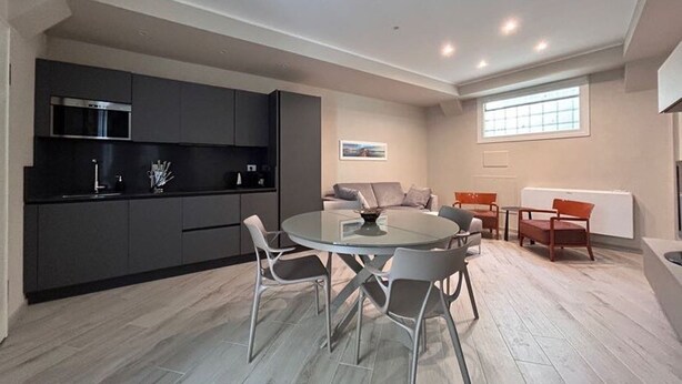 A modern kitchen with dark cabinets, a stainless steel microwave, and a round dining table with chairs. - Modern Apartment in the Heart of Pisa (Pisa)