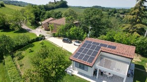 A modern house with a solar panel roof, a patio with outdoor seating, and a view of the surrounding countryside. - Villetta Monte San Lorenzo (Monte San Pietro)