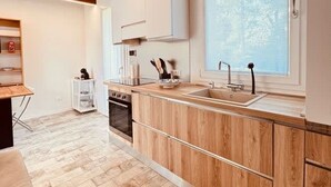 A modern kitchen with wooden cabinets, a large window, and a herringbone-patterned floor. - Villetta Monte San Lorenzo (Monte San Pietro)