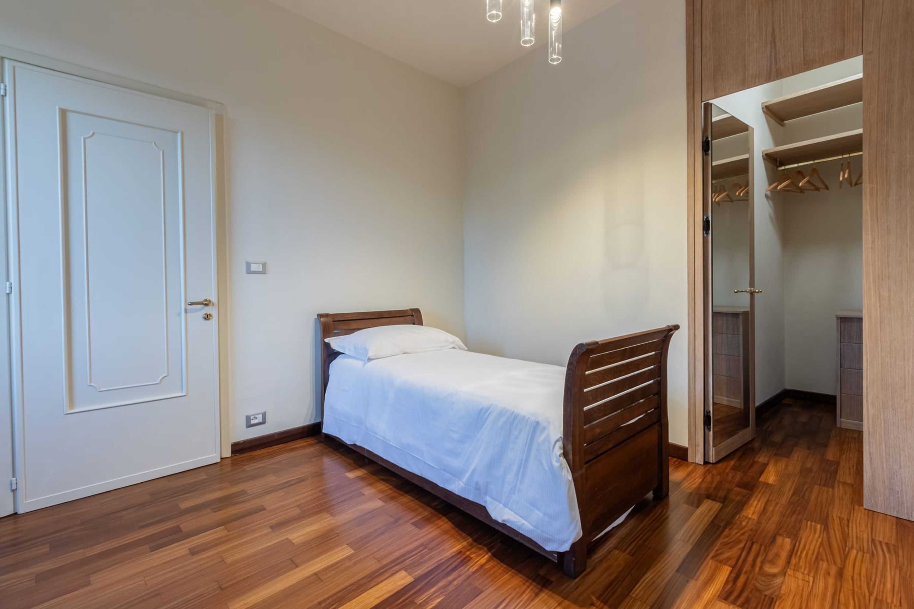 A bedroom with a wooden bed, a white door, and a walk-in closet with hanging space.