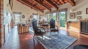 Un salon spacieux avec un haut plafond en bois, un canapé à motifs, deux fauteuils, une table basse et un grand tapis.