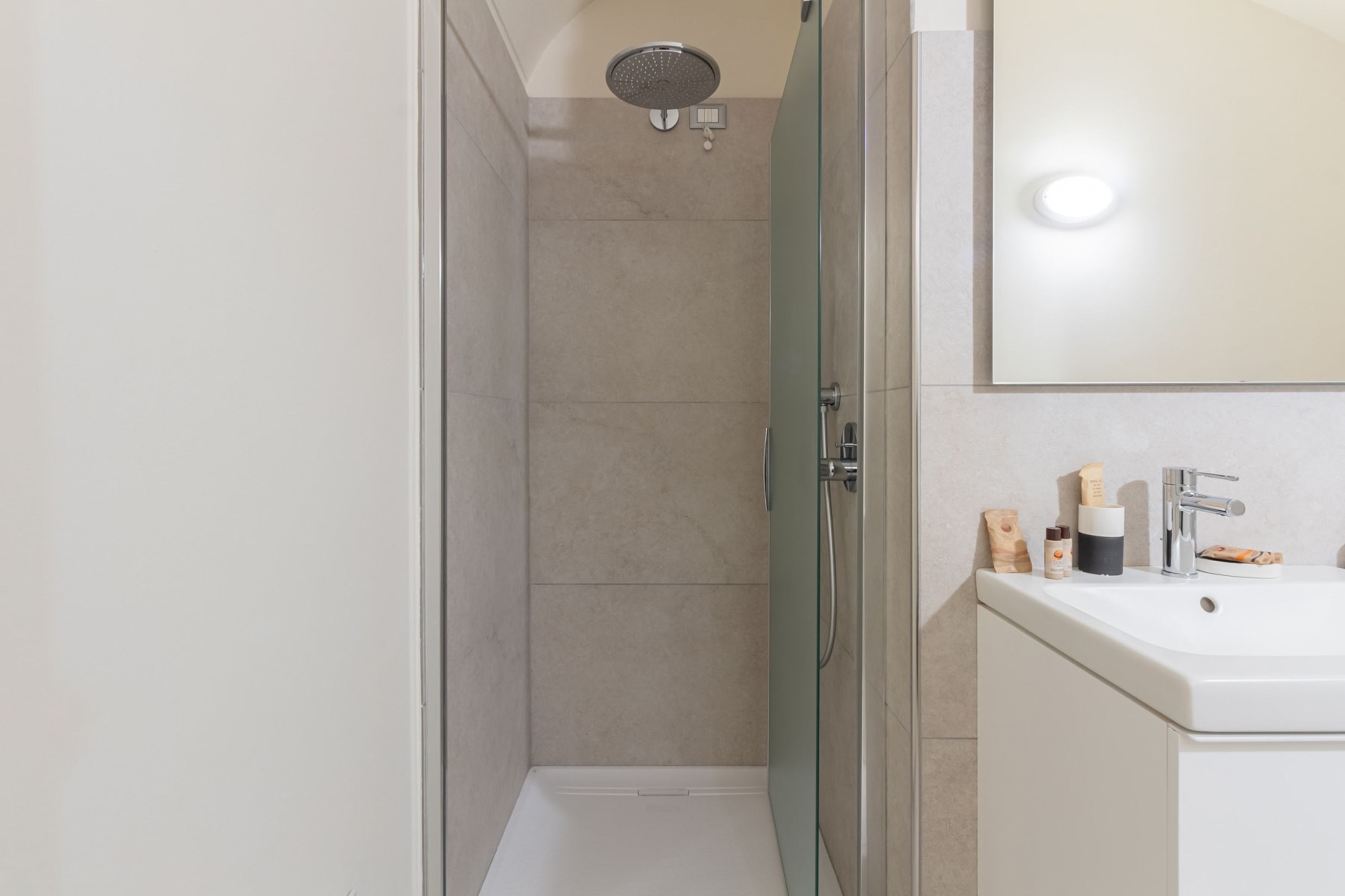 A modern bathroom with a glass shower enclosure, a white sink, and a mirror above it.