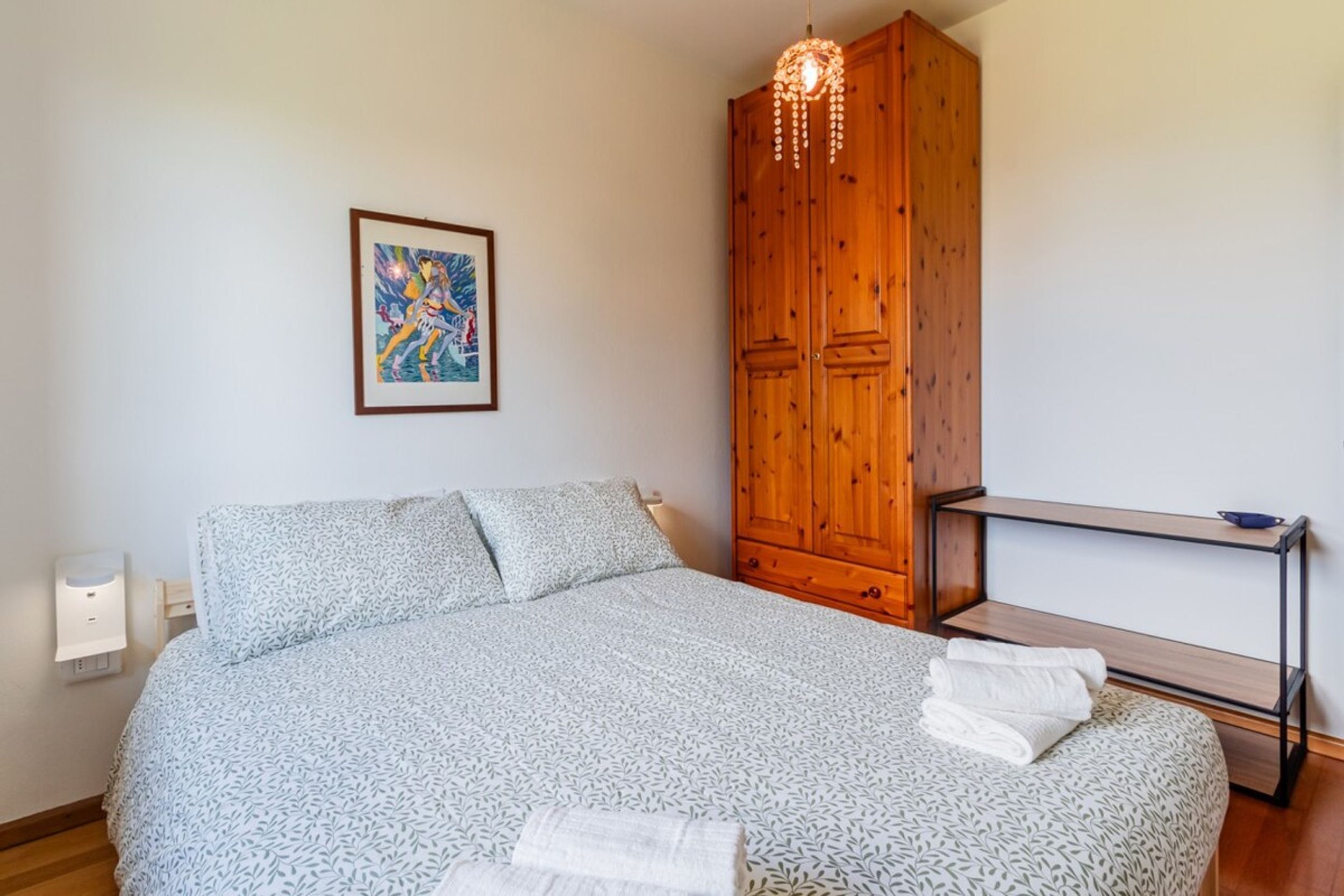 Ein Schlafzimmer mit einem Bett, einem Holzschrank, einem Nachttisch und einer Wandleuchte.