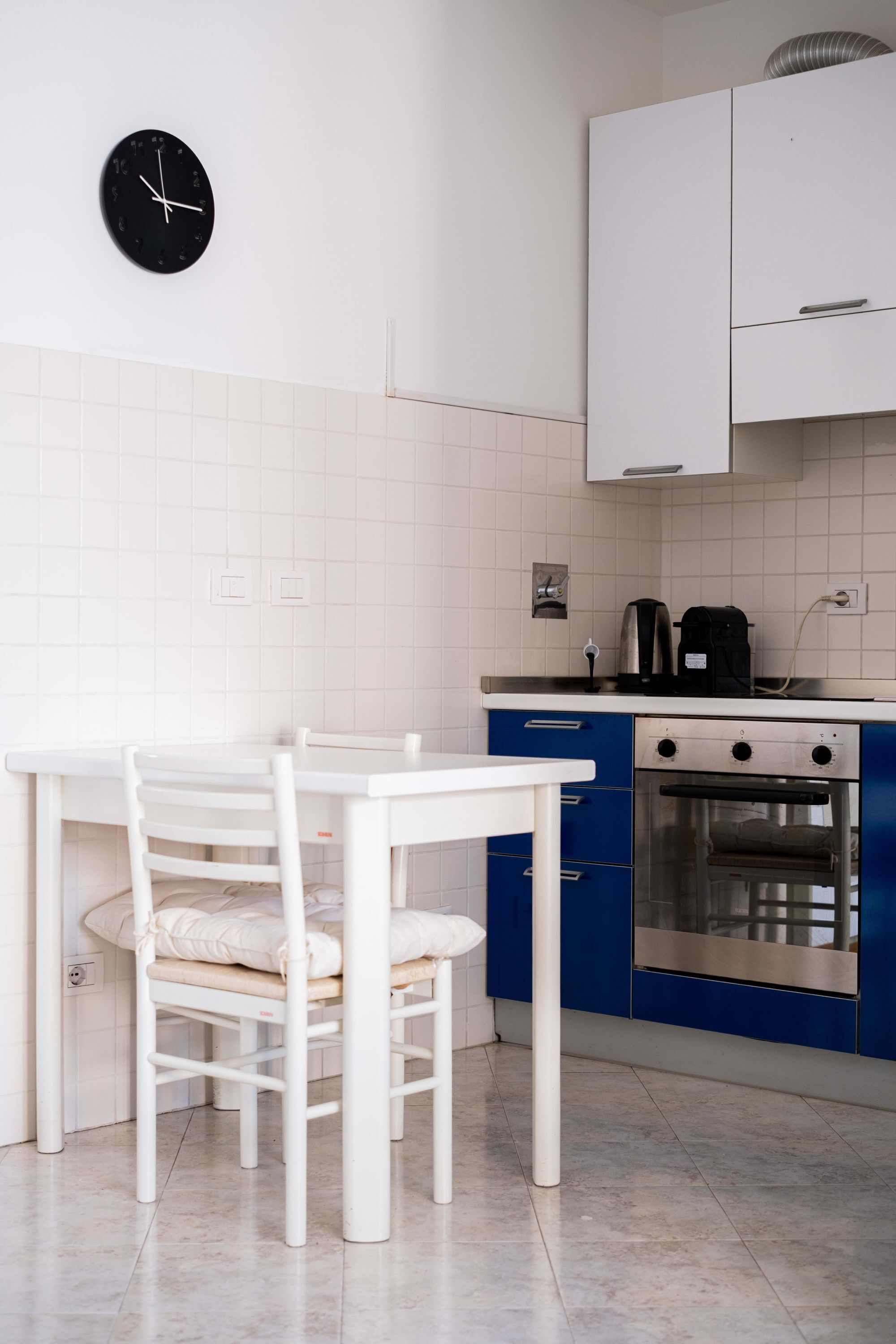 A kitchen with a white table and chairs, a clock, a stove, and cabinets.
