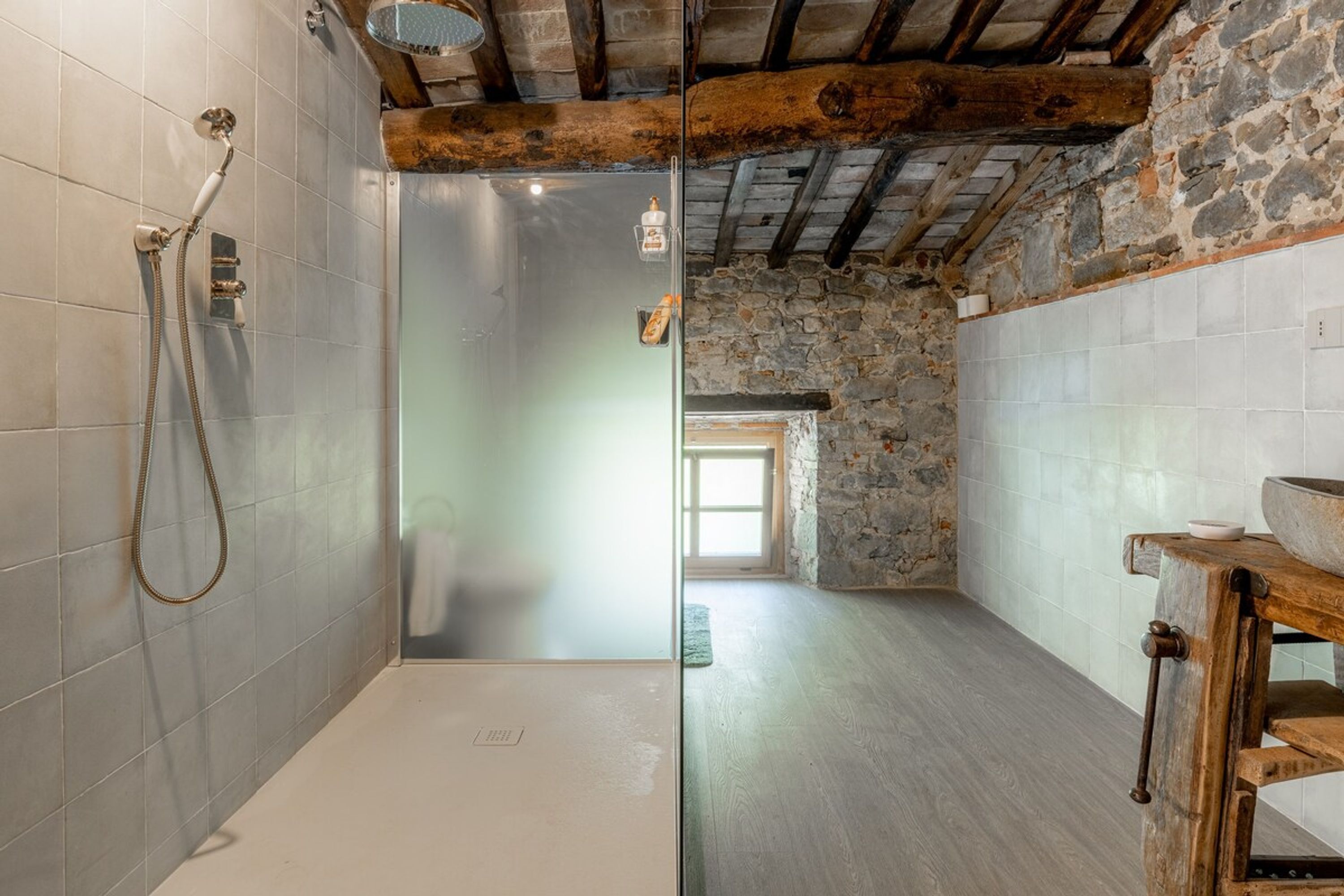 A bathroom with a shower, a stone wall, and a wooden beam ceiling.