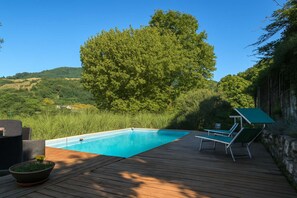 A wooden deck with a swimming pool, lounge chairs, and a large tree in the background. - Podere il Giardino Lucca - With Private Pool (Pescaglia)