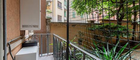 A balcony with a metal railing, a utility box, and a view of a building with balconies and greenery.
