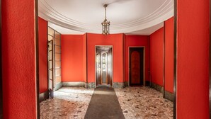 Un corridoio con pareti rosse, pavimento decorato e una porta centrale che dà su un'altra stanza.