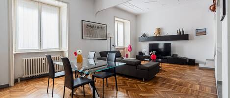 Un salon moderne avec une table à manger en verre, des canapés noirs et un téléviseur.