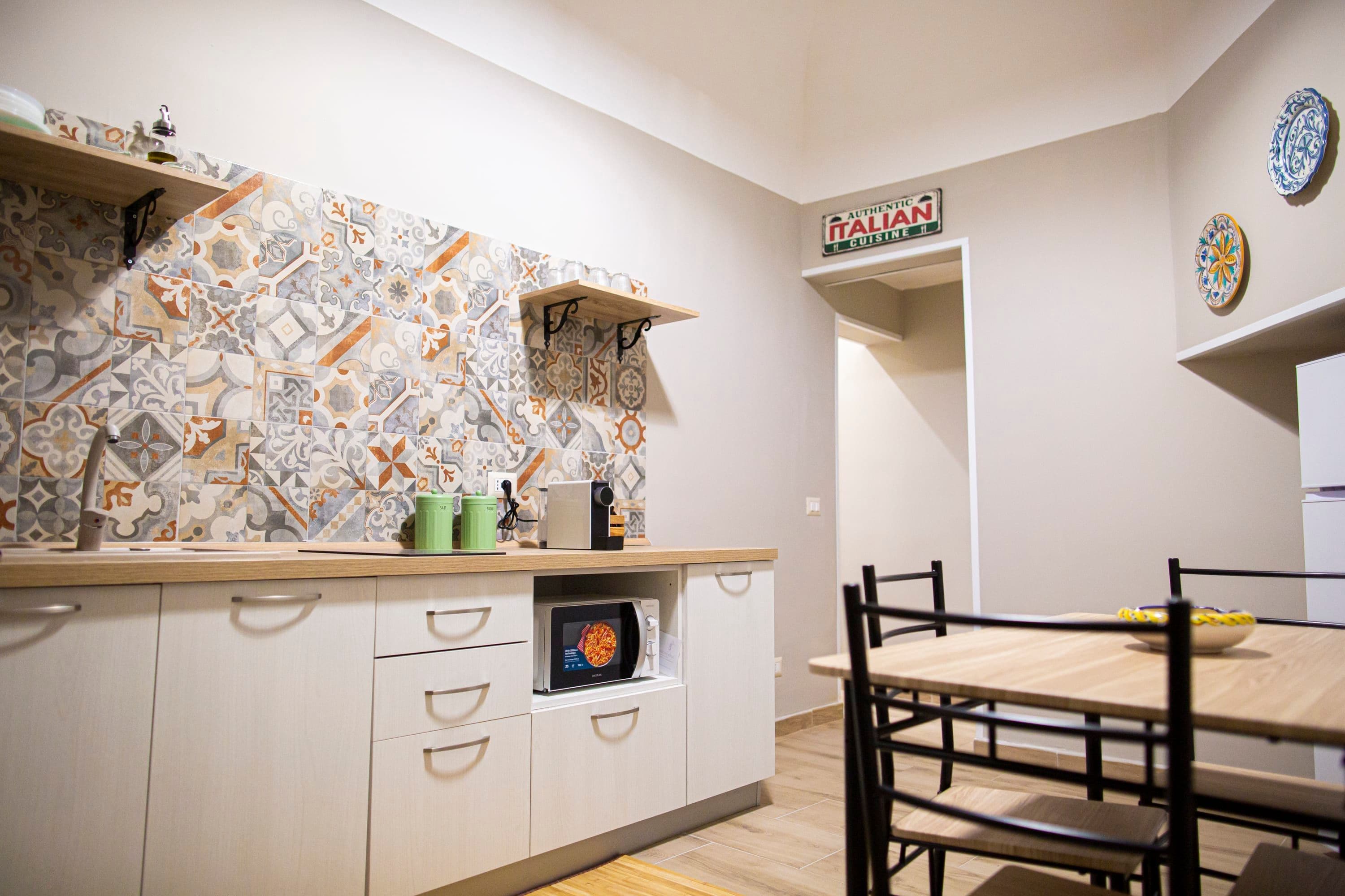 A kitchen with a patterned backsplash, a microwave, and a dining area with a table and chairs.