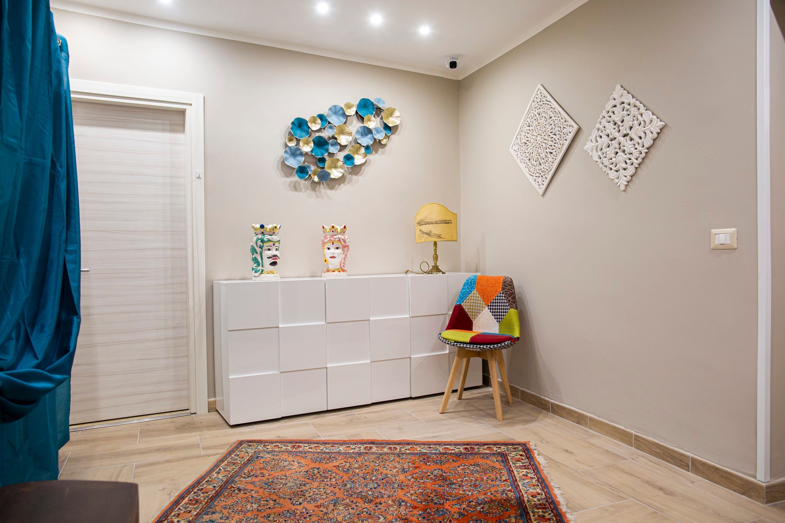 A room with a white cabinet, a colorful chair, a patterned rug, and decorative wall art.