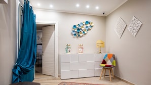 Una habitación con un mueble blanco para guardar objetos, una silla colorida y un tapete estampado.