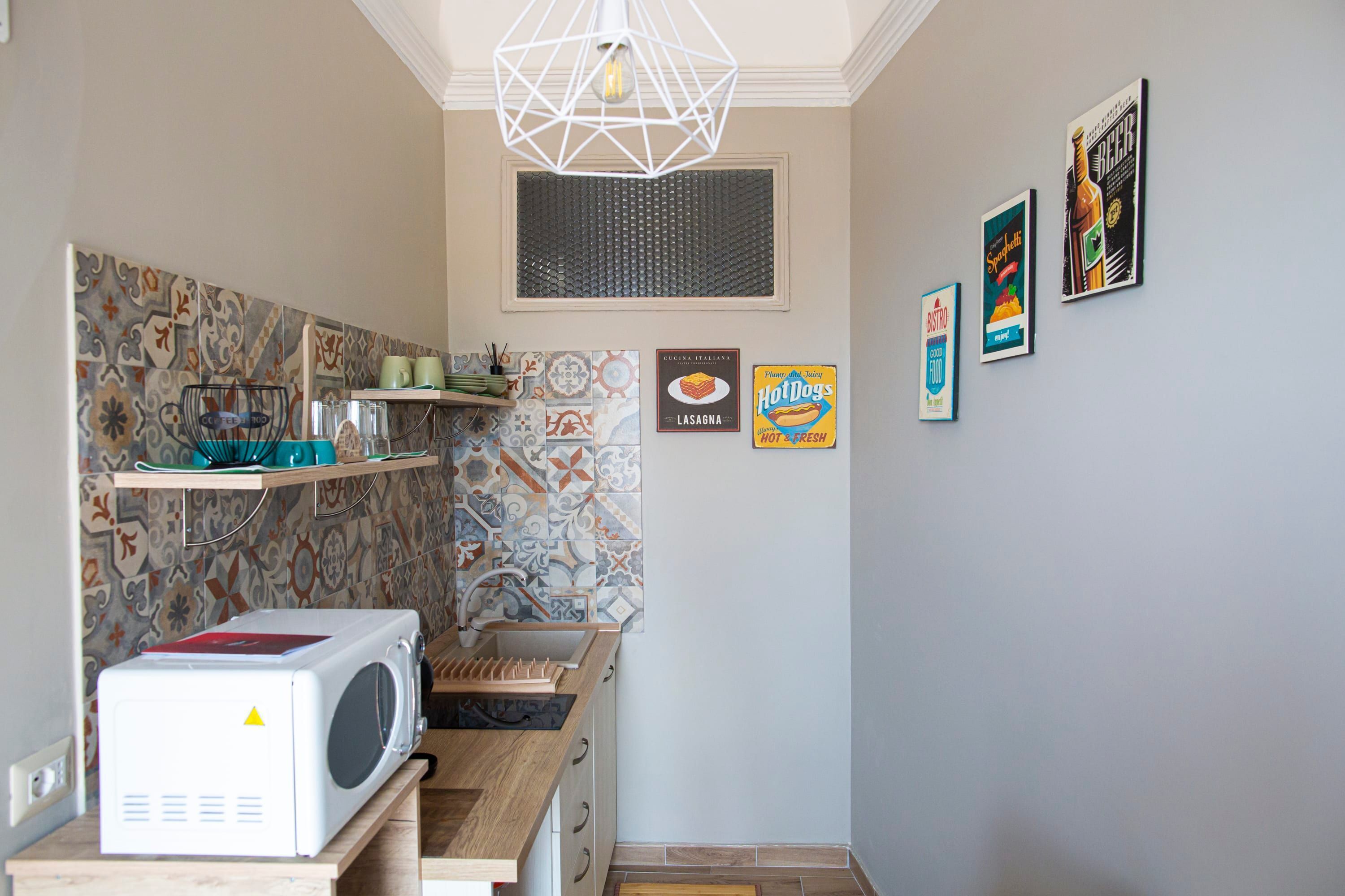 Een kleine keuken met een magnetron, planken en een hanglamp.