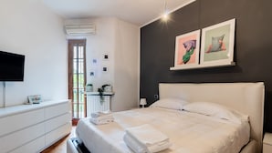 Ein modernes Schlafzimmer mit einem großen Bett, einer weißen Kommode und einem Flachbildfernseher an der Wand.
