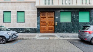 Egy épület, amelynek fából készült, kétszárnyú bejárati ajtaja, zöld zsaluzatai és fehér korláttal ellátott erkélye van.