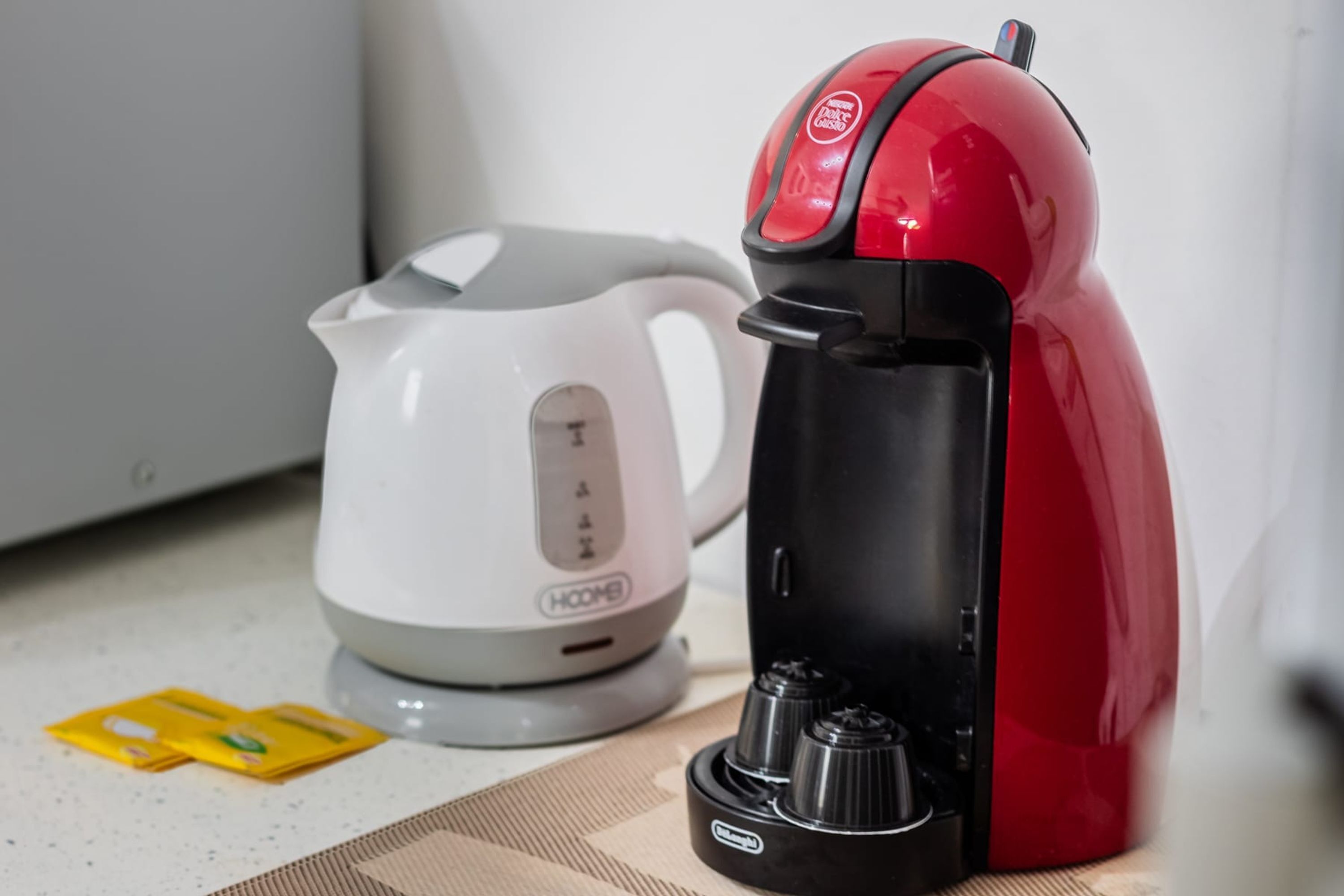 A red and black coffee maker and a white electric kettle on a kitchen counter.