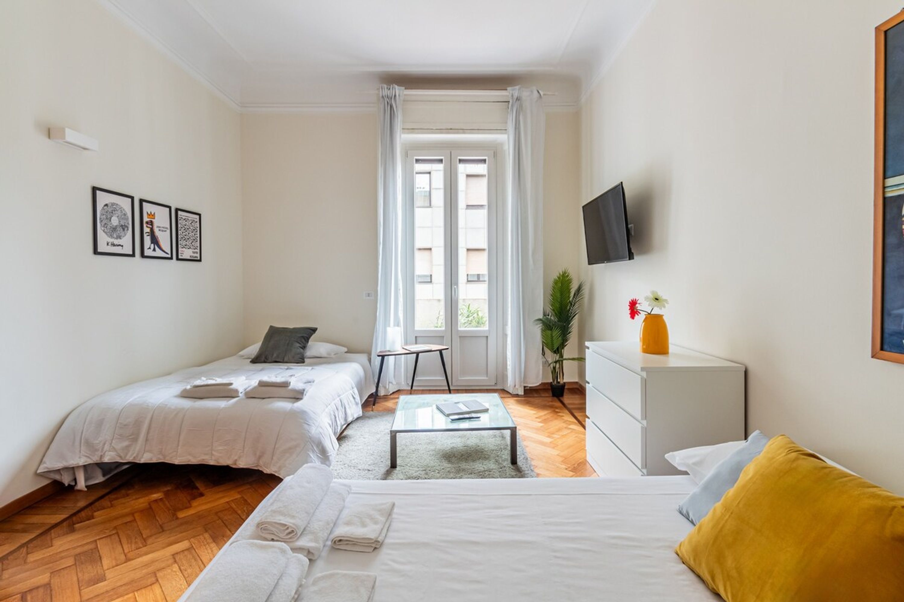 A hotel room with two beds, a small table, a TV, and a window with curtains.
