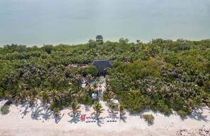 An aerial view of a resort with a pool, lounge chairs, and a thatched-roof building surrounded by dense vegetation and a beach. - ANANA Casa Cantarena (Tulum)