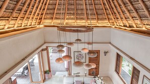 A spacious living area with a high ceiling and thatched roof, featuring a sofa set, dining table, and pendant lights. - ANANA Casa Cantarena (Tulum)
