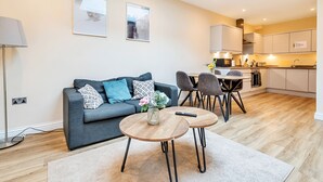 A modern living room with a grey sofa, a round wooden coffee table, and a dining area with a small table and chairs. - London Street Apt By REDWOOD STAYS (Basingstoke)