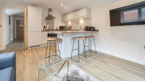 A modern kitchen with a microwave, coffee maker, and bar stools. There is a sign on the wall and a door leading to another room. - London Street Apt By REDWOOD STAYS (Basingstoke)