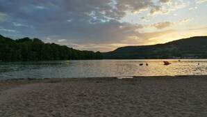 Ein Strand mit sandigem Ufer und ruhigem Wasser, umgeben von Hügeln und Bäumen.