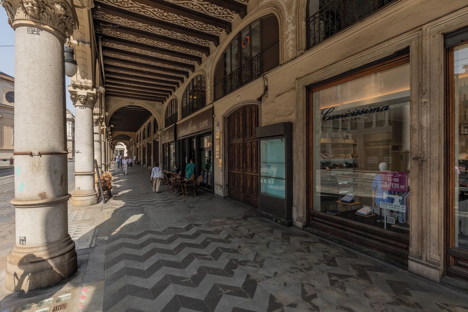 An indoor corridor with classical architecture, including ornate columns and a patterned floor.