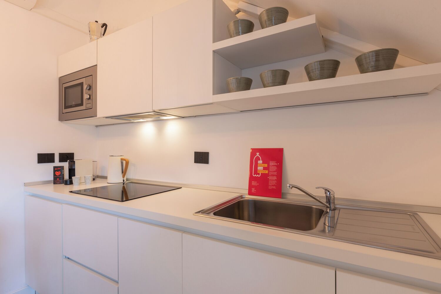 A modern kitchen with white cabinetry, a stainless steel sink, a microwave, and a coffee machine.