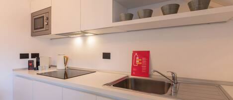 A modern kitchen with white cabinetry, a stainless steel sink, a microwave, and a coffee machine.