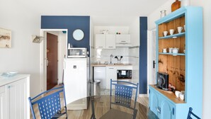 Una cocina compacta con armarios blancos, un microondas y una cafetera. Hay una mesa de comedor con sillas azules.