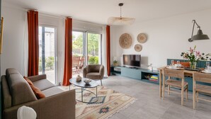 A modern living room with a sofa, a dining table with chairs, a TV, and a large window with curtains. - Les Sternes - Appt proche de la plage (Saint-Malo)
