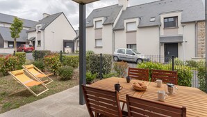 A patio with a wooden table and chairs, a small garden, and a view of neighboring houses. - Les Sternes - Appt proche de la plage (Saint-Malo)