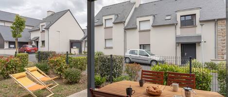 A patio with a wooden table and chairs, a small garden, and a view of neighboring houses.