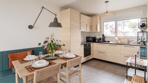A modern kitchen with wooden cabinets, a dining table set for four, and a large window providing natural light. - Les Sternes - Appt proche de la plage (Saint-Malo)