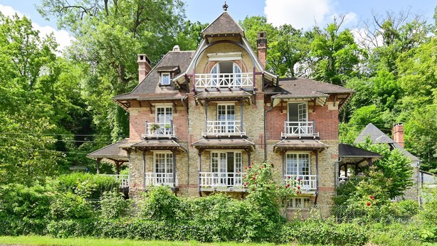 Ein großes, mehrstöckiges Haus mit einem zentralen Turm, umgeben von üppiger Vegetation.