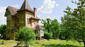 Ein großes Steinhaus mit einem steilen Dach und einer kleinen Holzhütte im Vordergrund.