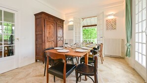 Ein Esszimmer mit einem großen Holztisch, gedeckt für sechs Personen, flankiert von hohen Schränken und einem Fenster mit Vorhängen.