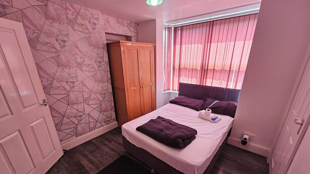 Een slaapkamer met een bed, een kledingkast, een raam met gordijnen en een deur.