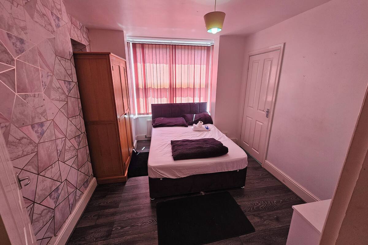 A bedroom with a bed, a wardrobe, a radiator, and a window with curtains.