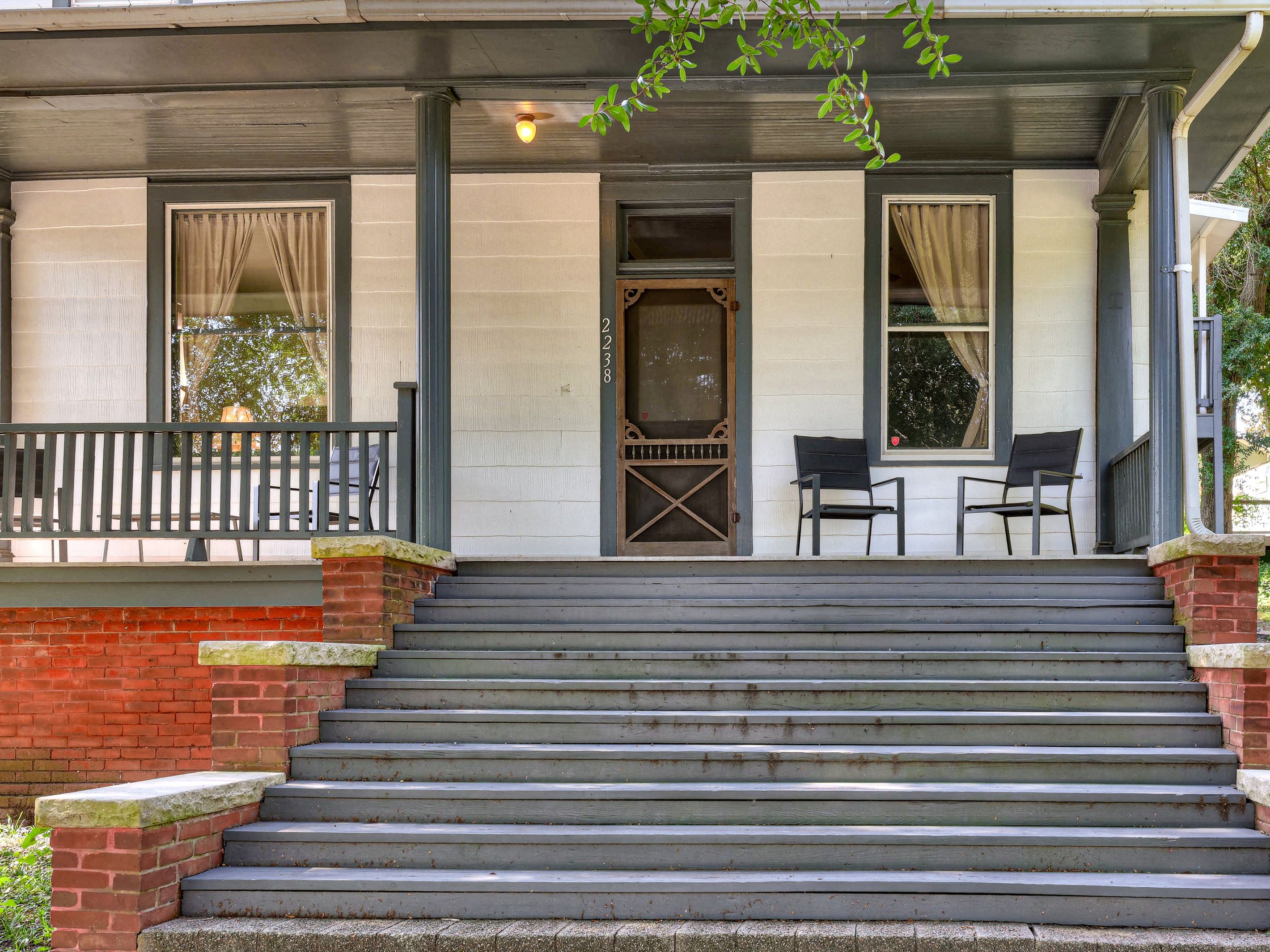 A two-story building with a front porch, a set of stairs leading to the entrance, and two chairs on the porch.
