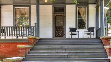 A two-story building with a front porch, a set of stairs leading to the entrance, and two chairs on the porch.