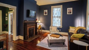 Una sala de estar con chimenea, televisor montado en la pared, sofá y ventana con cortinas.