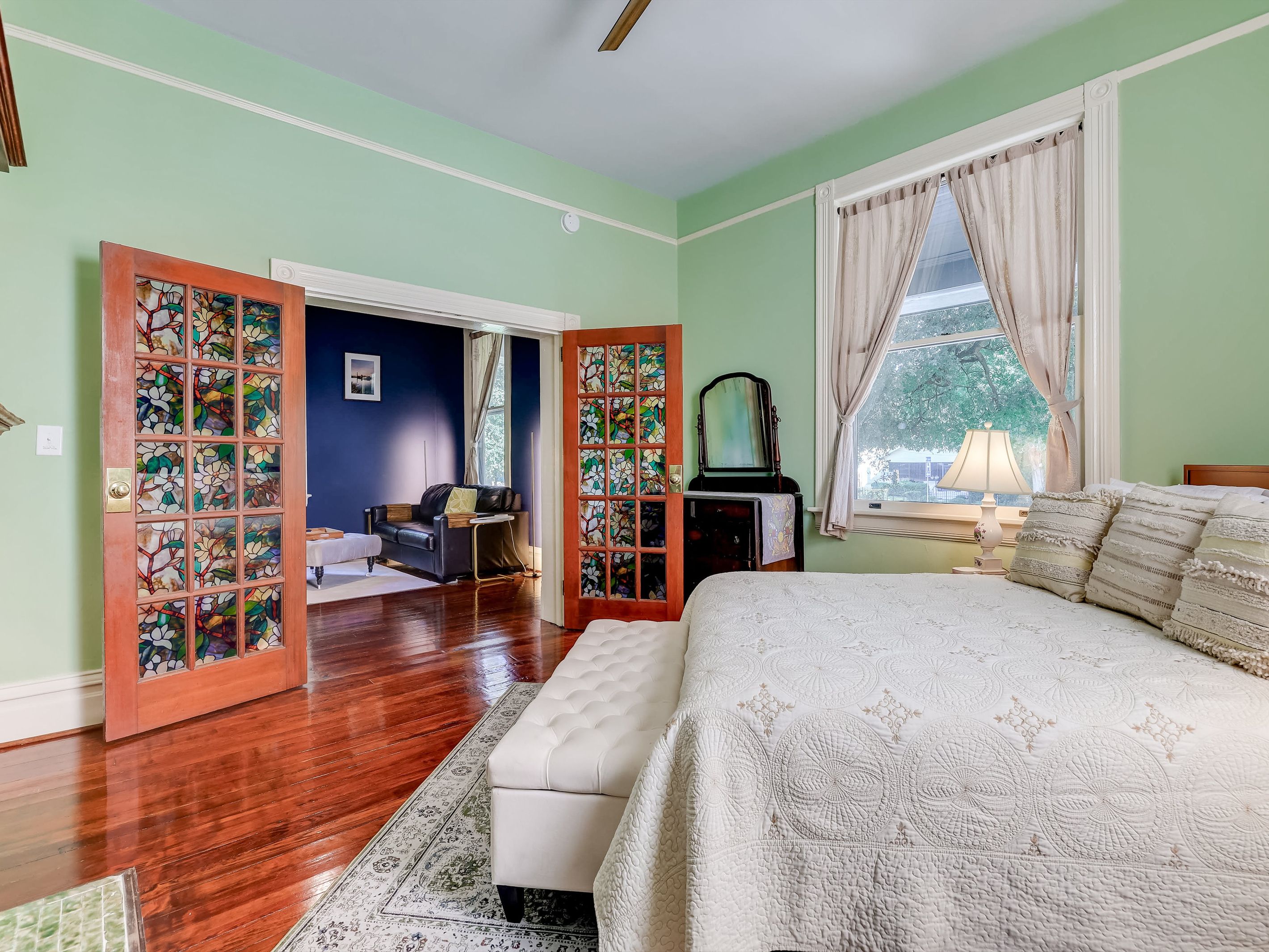 A bedroom with a large bed, a dresser, a mirror, and a window with curtains.