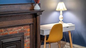 Una habitación con chimenea de ladrillo, un escritorio blanco, una silla de color mostaza y una lámpara.